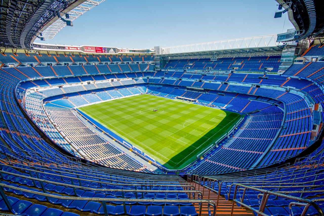 A wide-angle view of a large, empty sports stadium with blue seats and a green grass field.