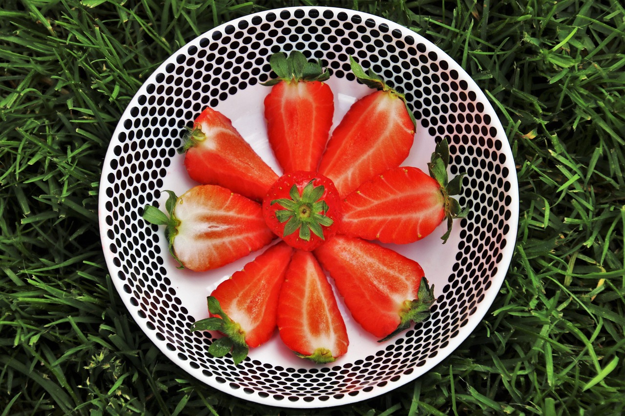 A bowl of sliced strawberries arranged in a flower pattern on a bed of grass.