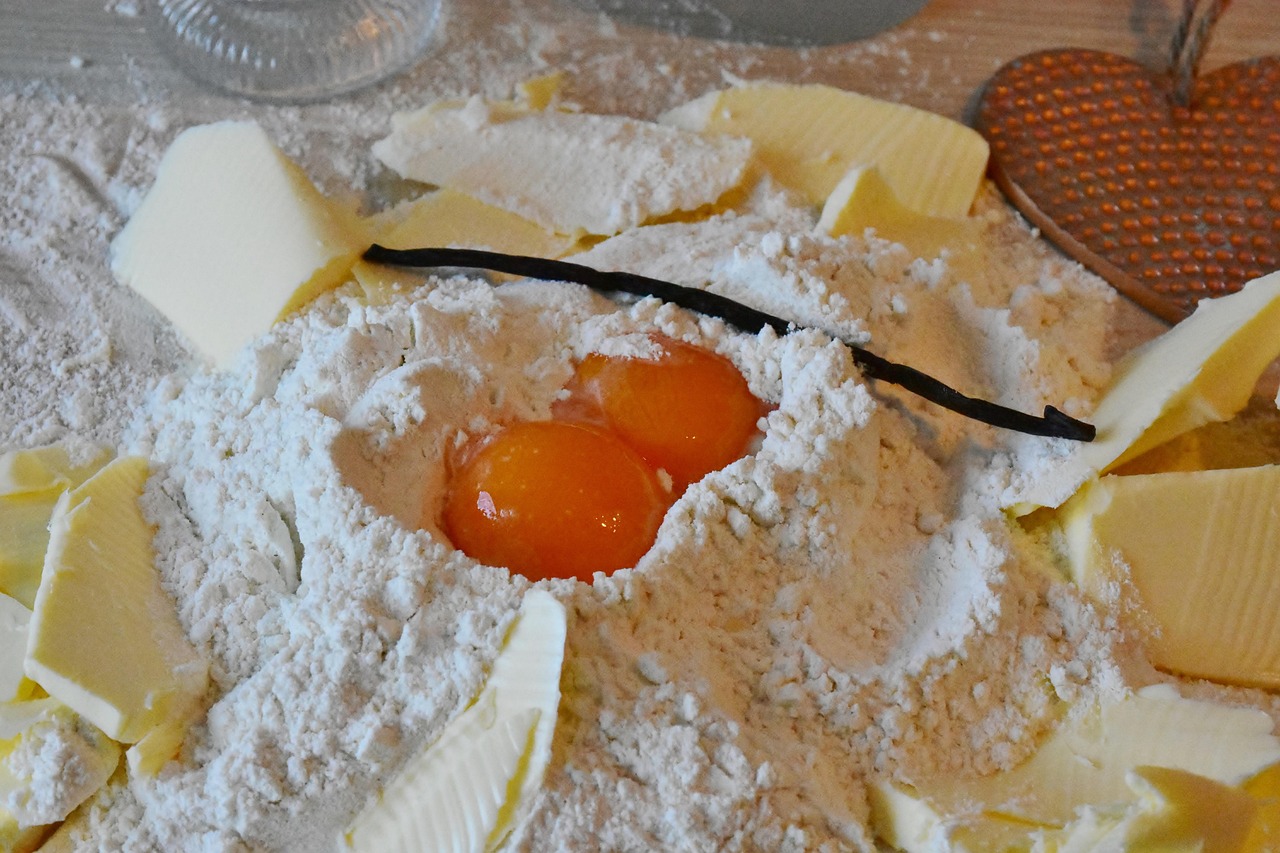A vanilla bean resting on a pile of flour, butter, and egg yolks, representing the ingredients for baking.