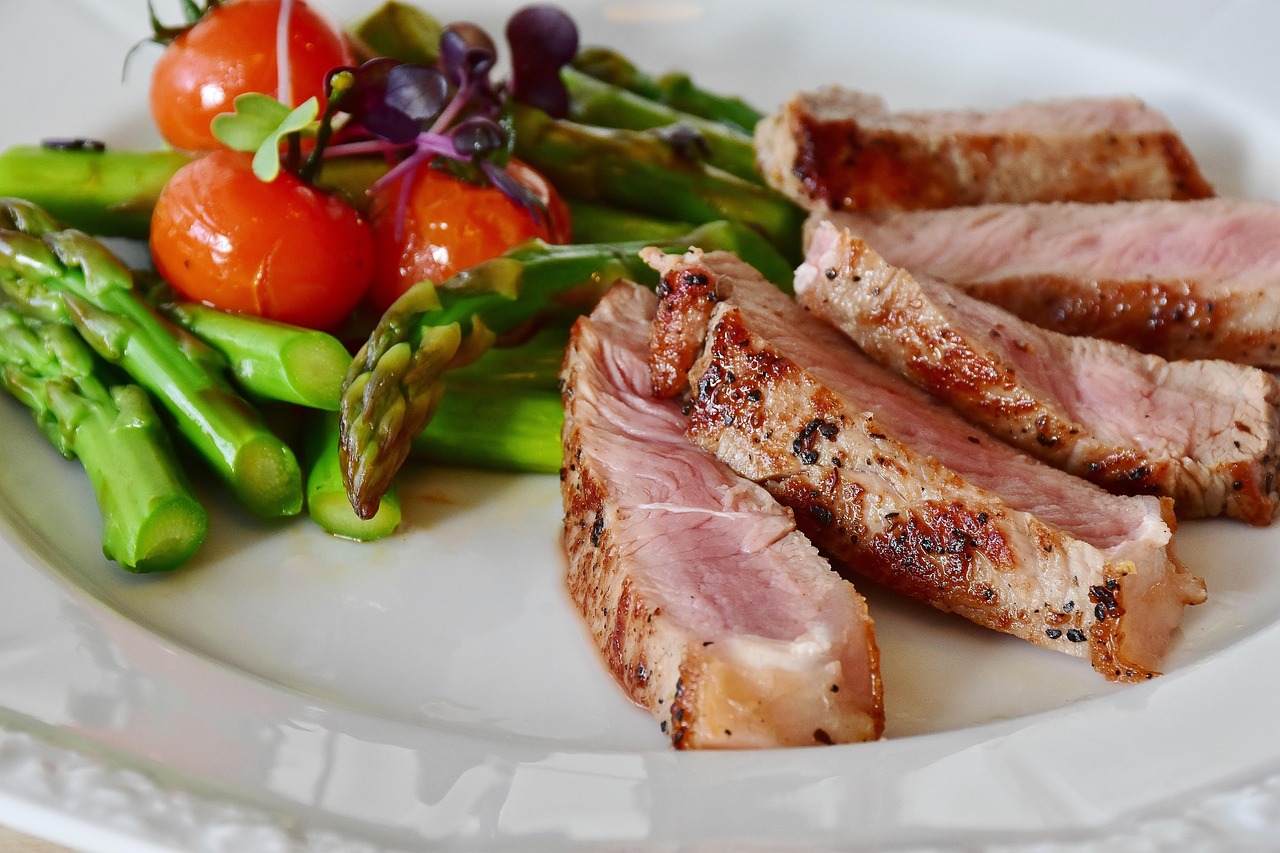 A plate featuring sliced steak, asparagus, and cherry tomatoes, representing a meal that could be analyzed for blood sugar impact.