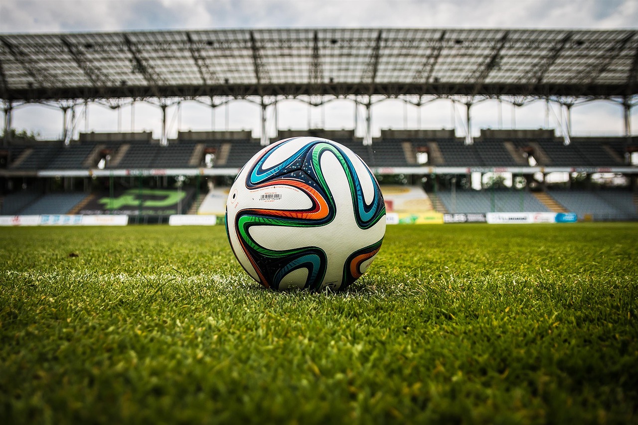 A soccer ball sits on the grass in the middle of an empty stadium.