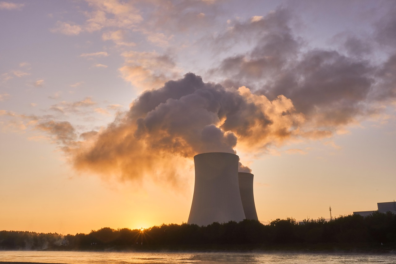 A nuclear power plant with cooling towers emitting steam against a sunset sky.