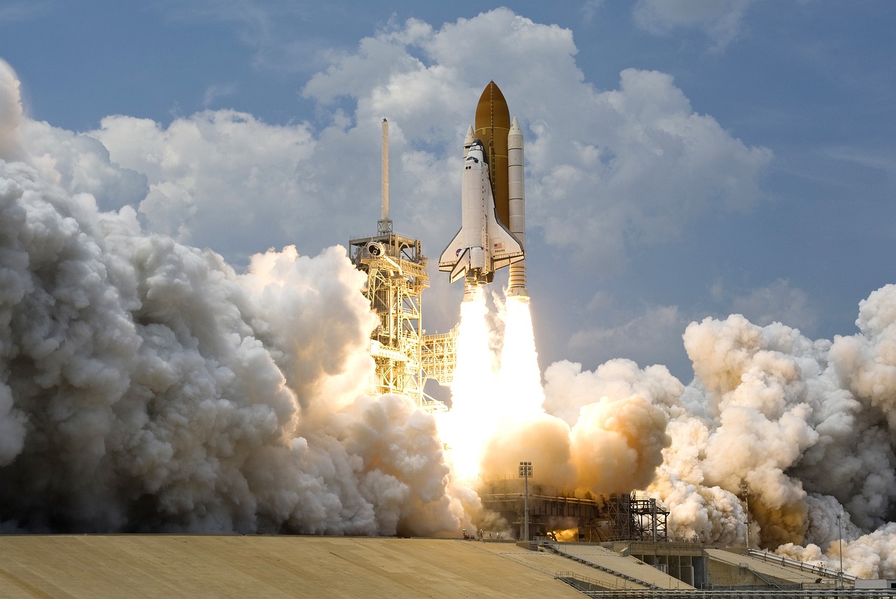 A space shuttle launching into the sky, surrounded by massive clouds of white smoke and exhaust.