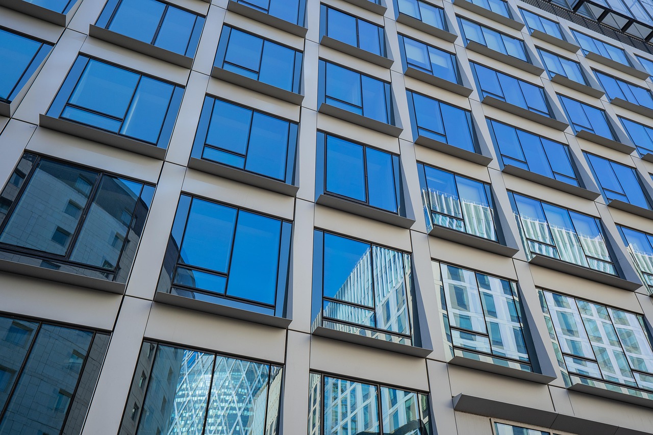 A modern office building with glass windows reflecting the sky and surrounding architecture.