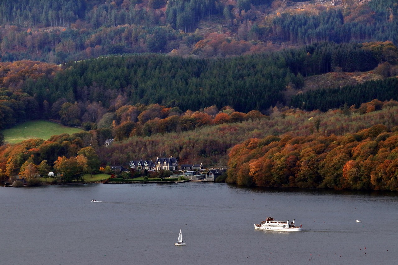 A scenic view of Windermere Lake with boats and autumn forests surrounding the water.