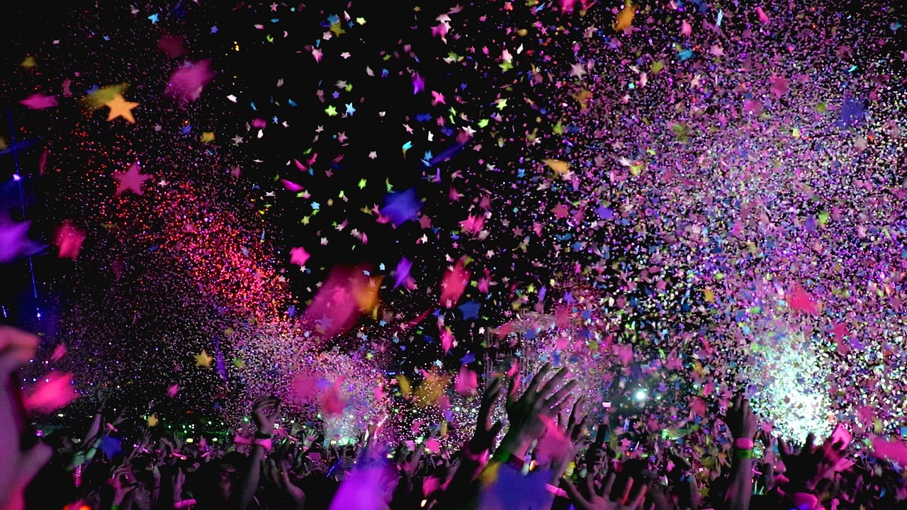 A festive crowd celebrating at a concert with colorful confetti and star-shaped paper falling through the air.