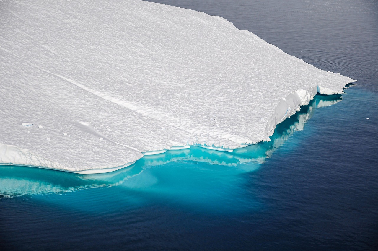 An aerial view of a large iceberg floating in deep blue Arctic waters.