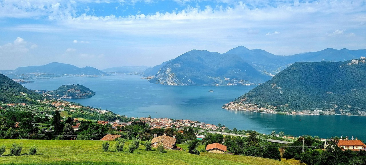 A wide panoramic view of a large Italian lake surrounded by mountains and small towns.