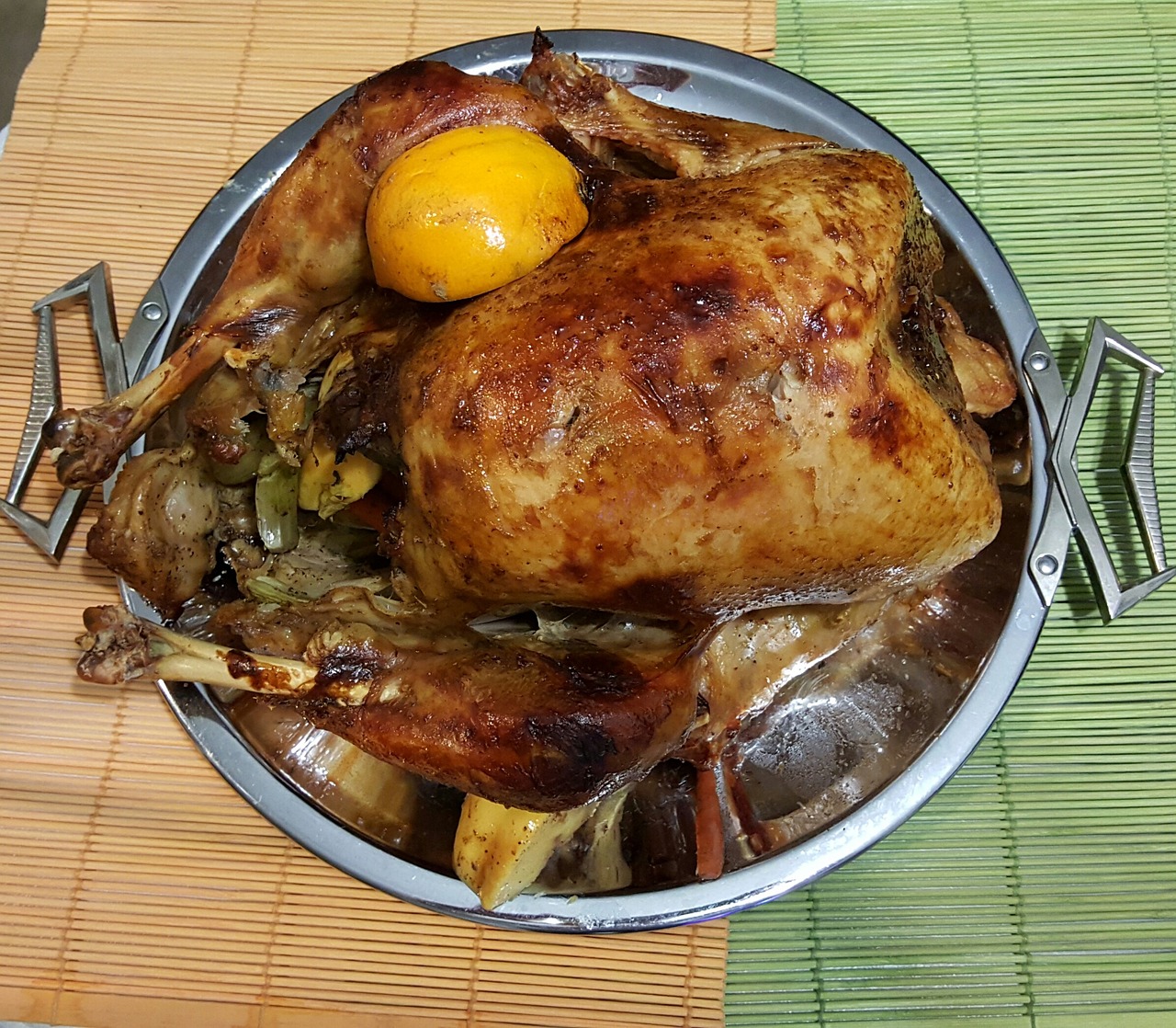 A roasted turkey on a metal platter with a lemon on top.