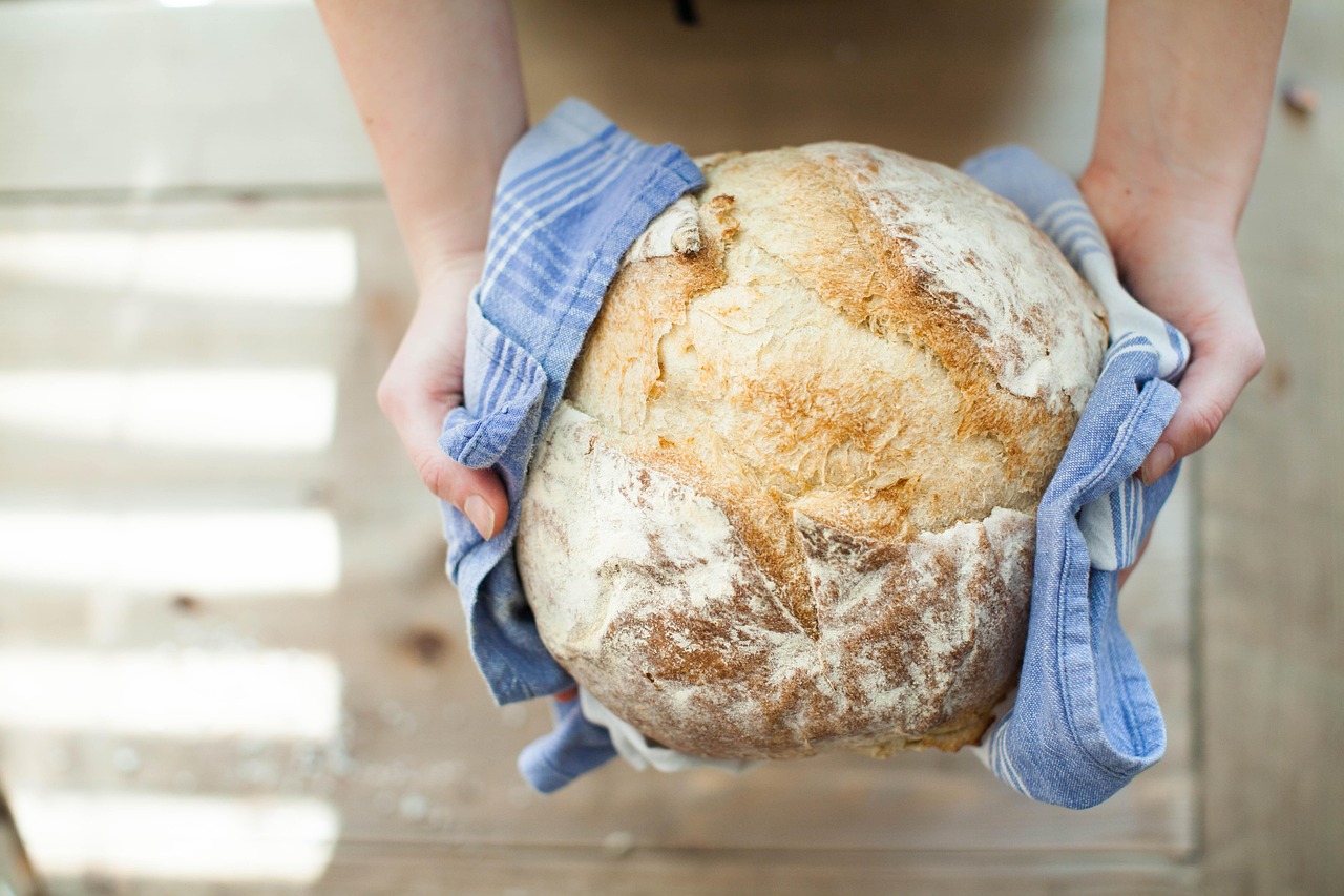 A person holding a freshly baked loaf of bread in a blue and white cloth.
