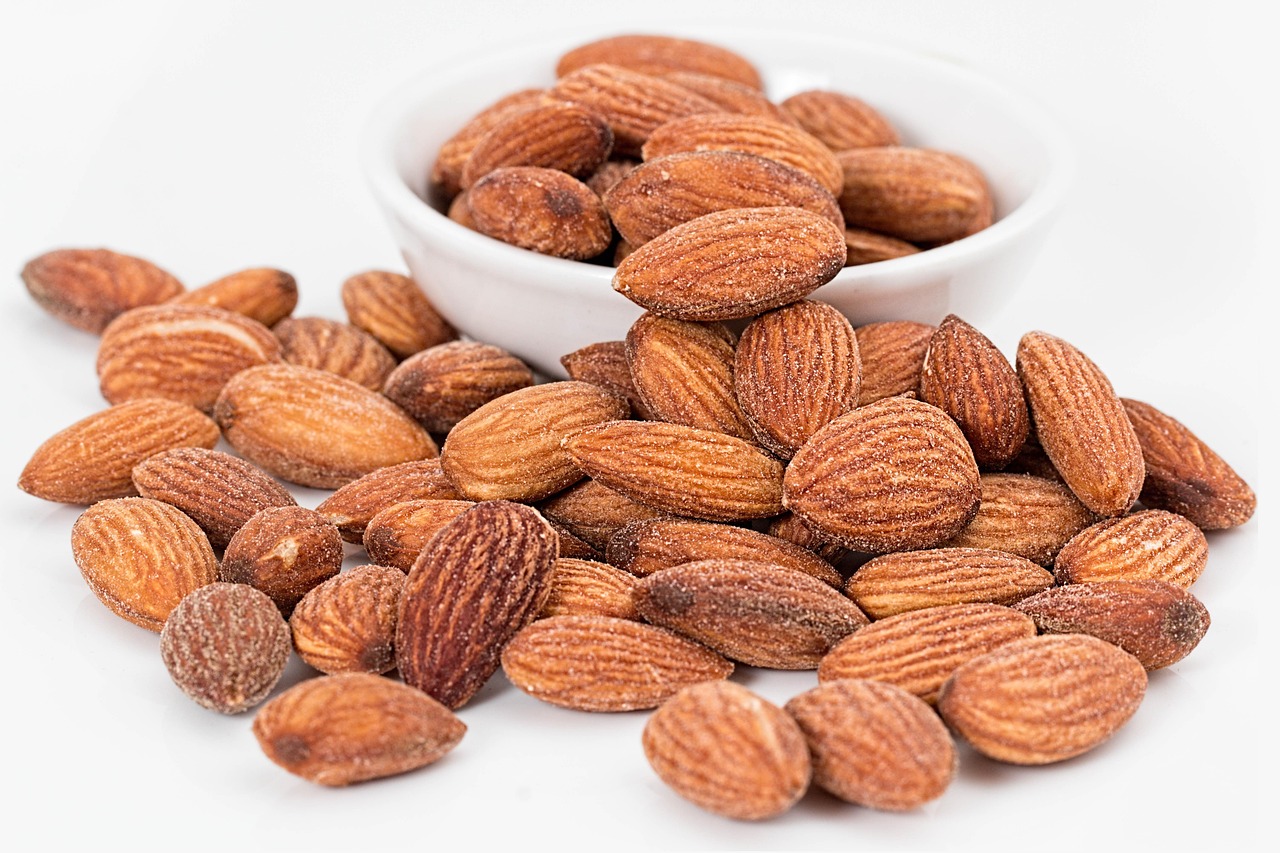 A bowl and a pile of almonds on a white background