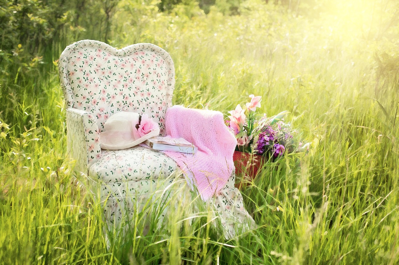 A floral patterned armchair placed in a sunny, grassy field, representing a shabby chic aesthetic.