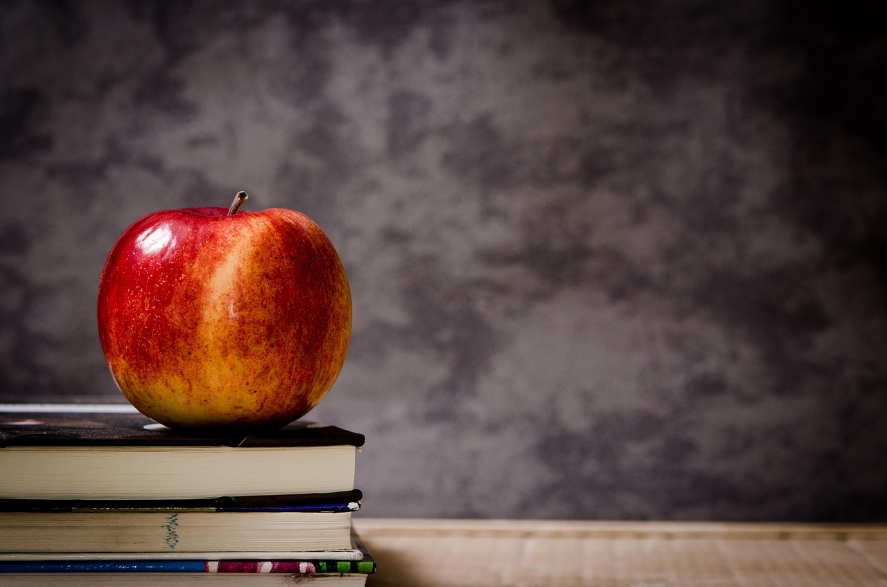 A red apple sitting on top of a stack of books, symbolizing school and health.