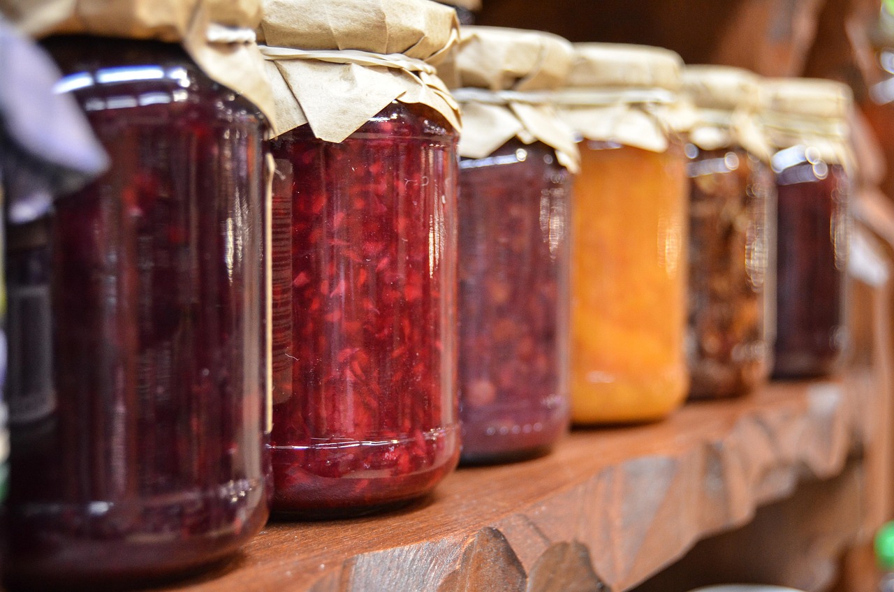 A row of glass jars filled with colorful preserves and jams sitting on a wooden shelf.