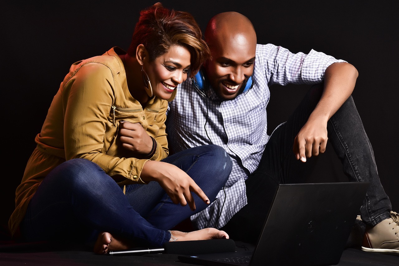 A man and a woman sitting together and looking at a laptop screen, representing digital media consumption.