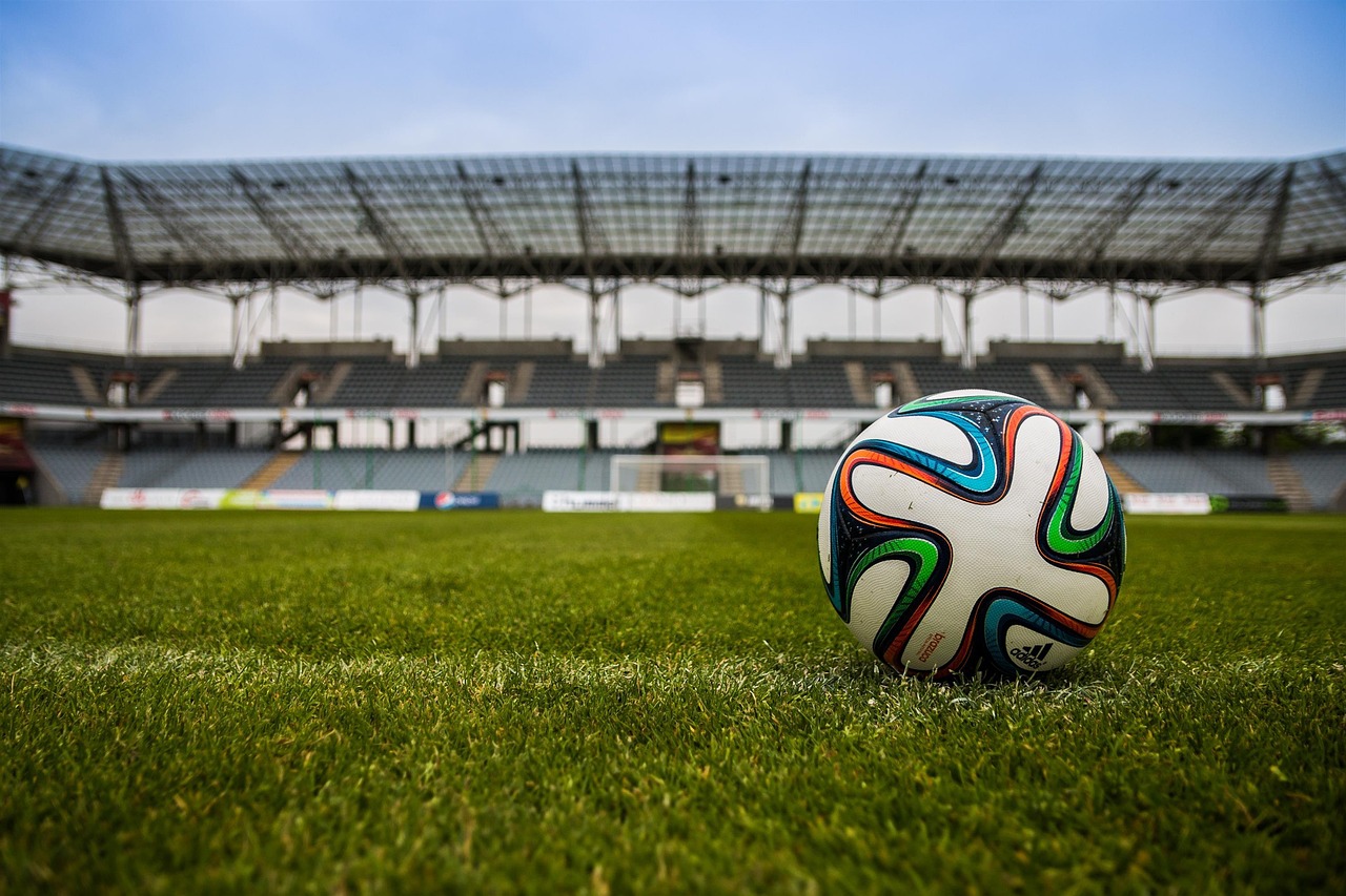 A soccer ball resting on the grass of a large, empty stadium.