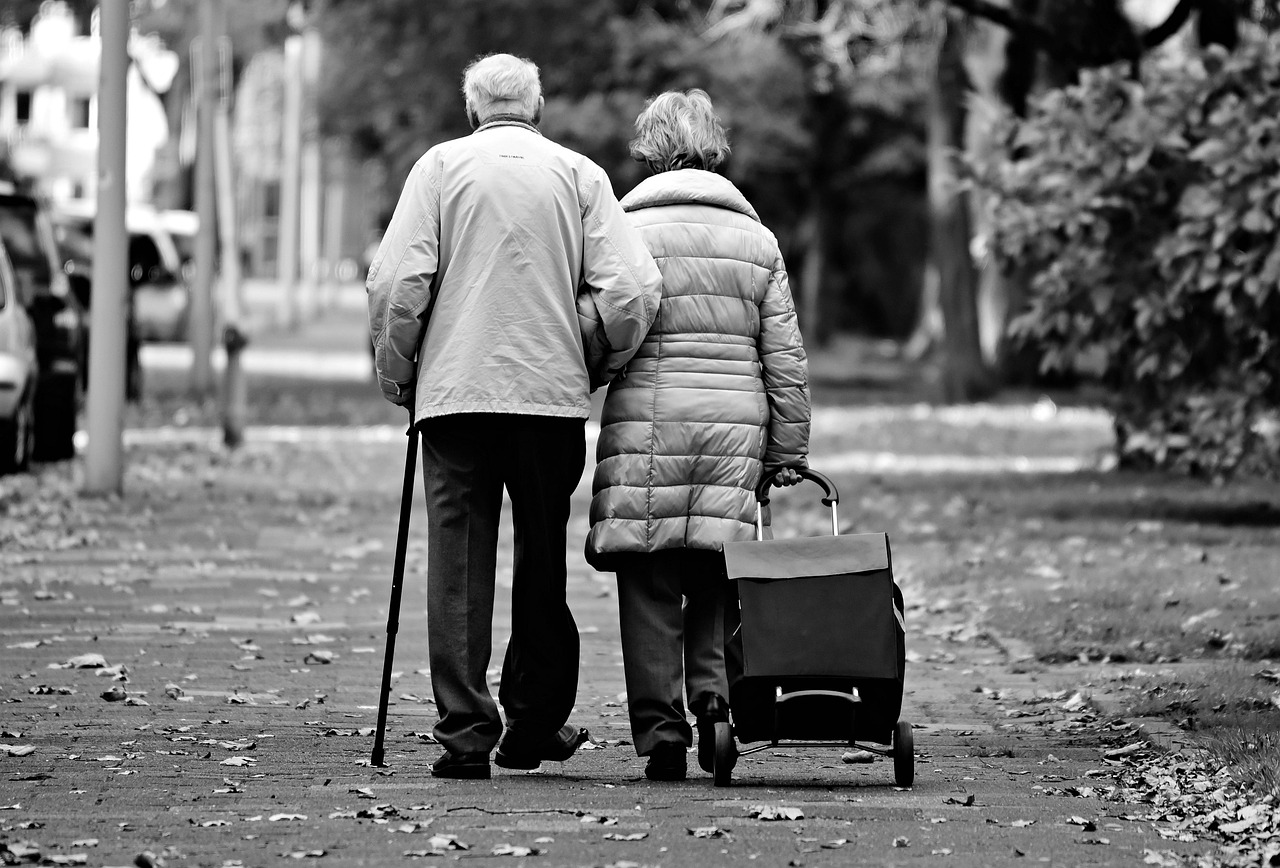 An elderly couple walking together on a path, seen from behind.