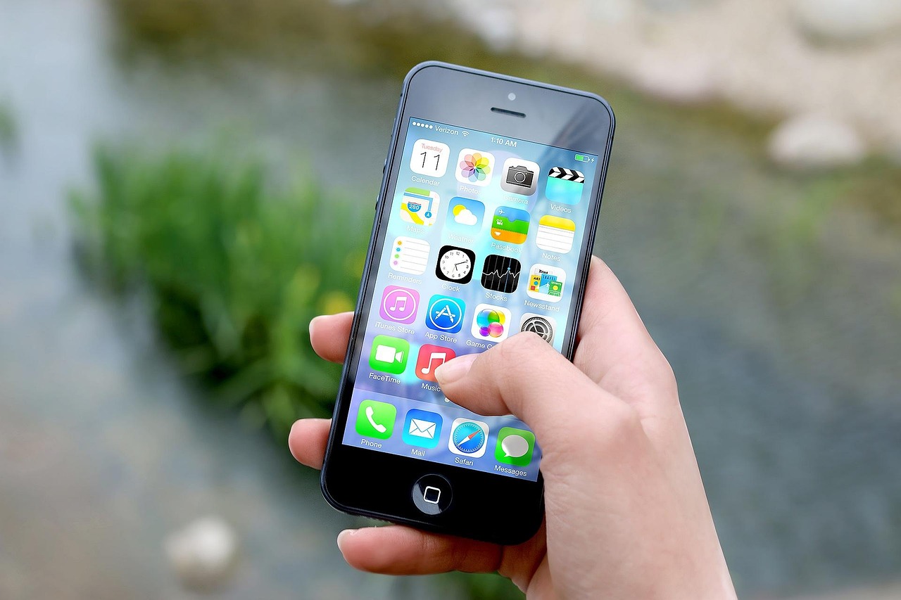 A person holding a smartphone displaying various app icons on the screen.