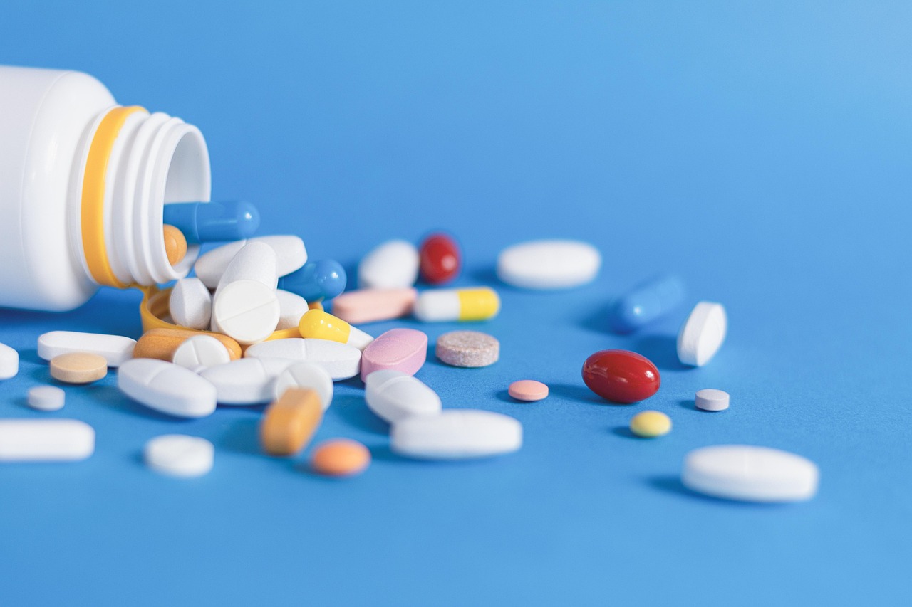 A white pill bottle lying on its side with various colorful pills and capsules scattered on a blue background.