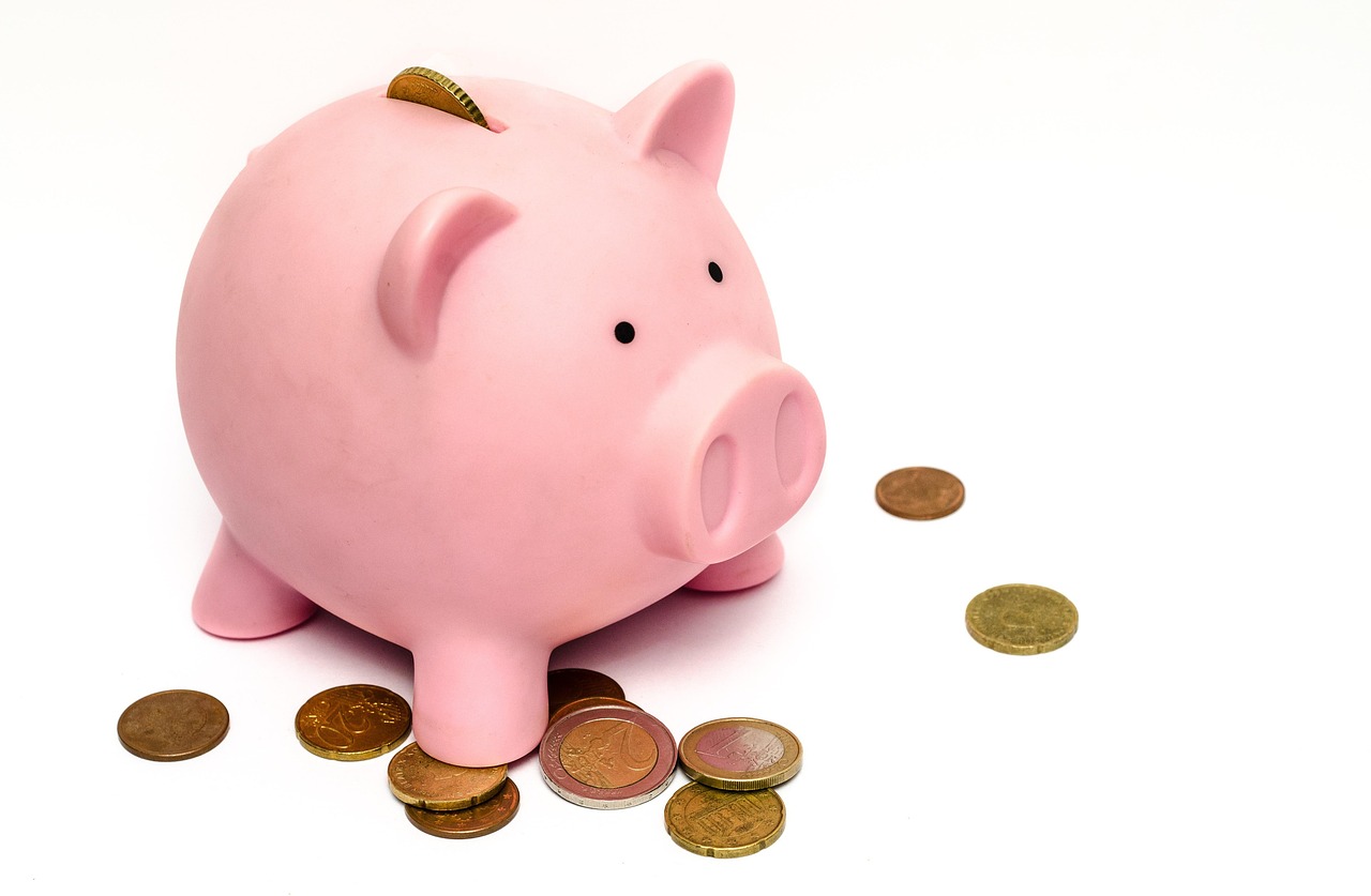 A pink piggy bank with a coin inserted in the slot and several coins scattered on the surface around it.