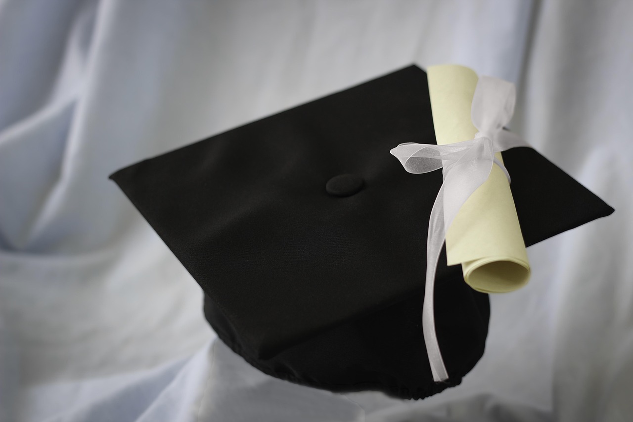 A black graduation cap with a rolled diploma tied with a white ribbon.