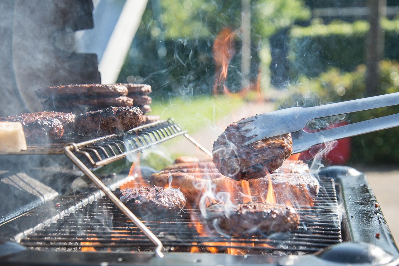 A close-up of hamburger patties being grilled over an open flame with tongs.