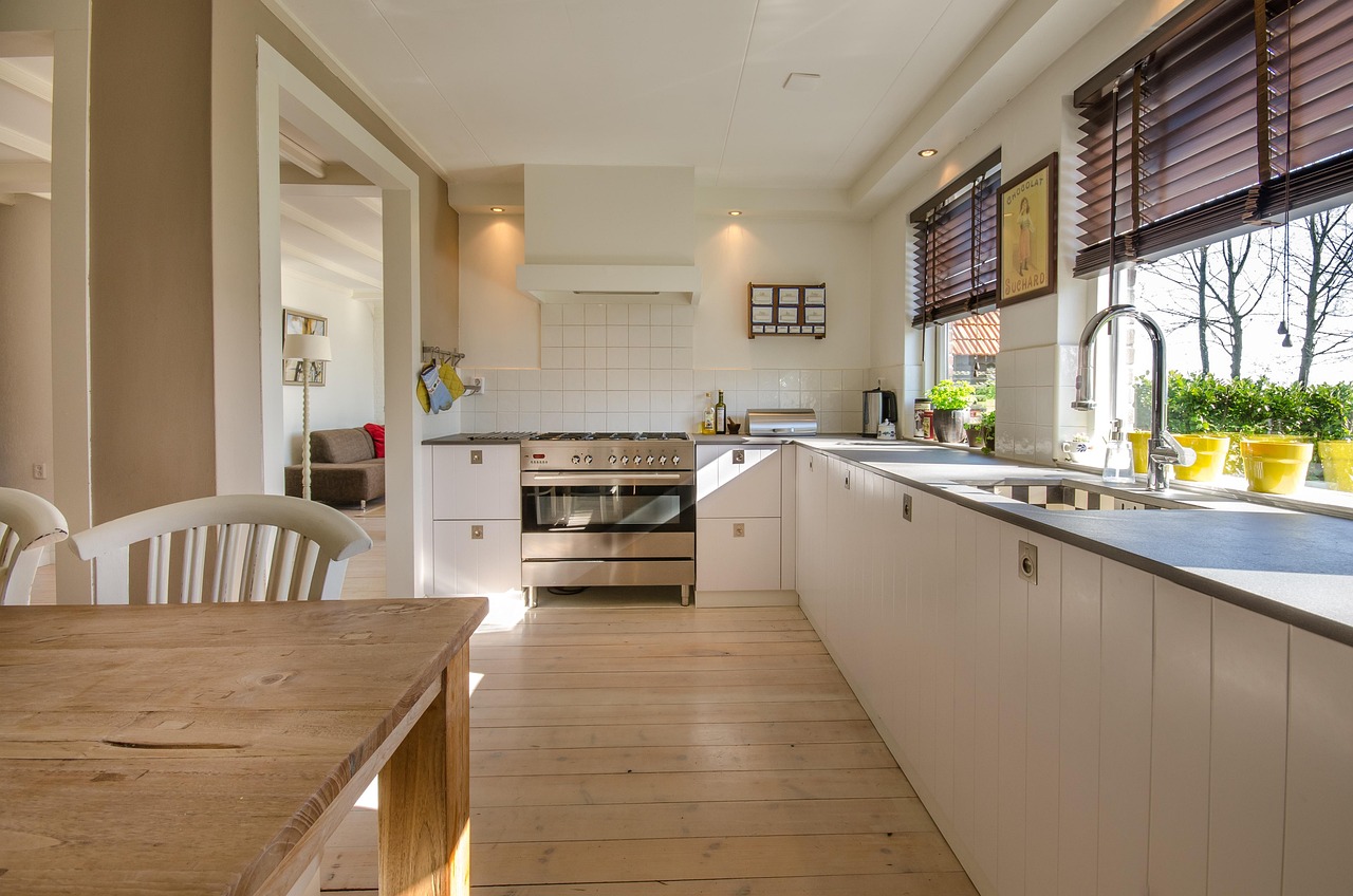A modern, well-lit kitchen with a wooden table in the foreground and a stainless steel stove and oven in the background.