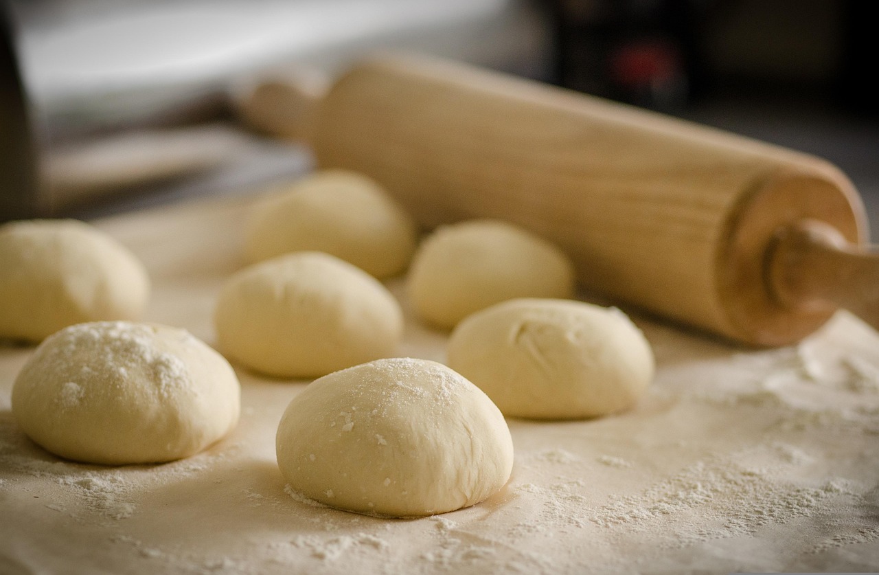 Several balls of dough on a floured surface with a wooden rolling pin in the background.