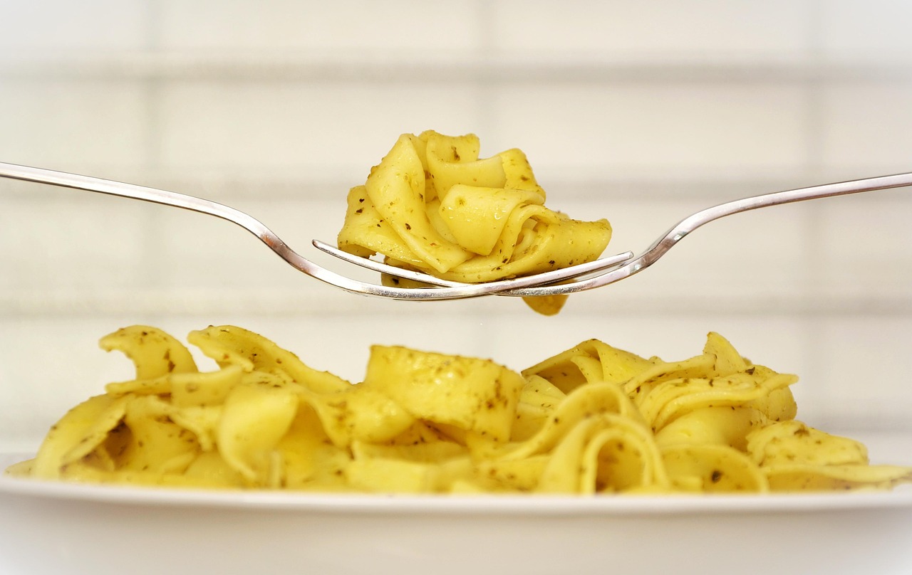 A close-up of a fork lifting a portion of pasta from a plate of pasta.