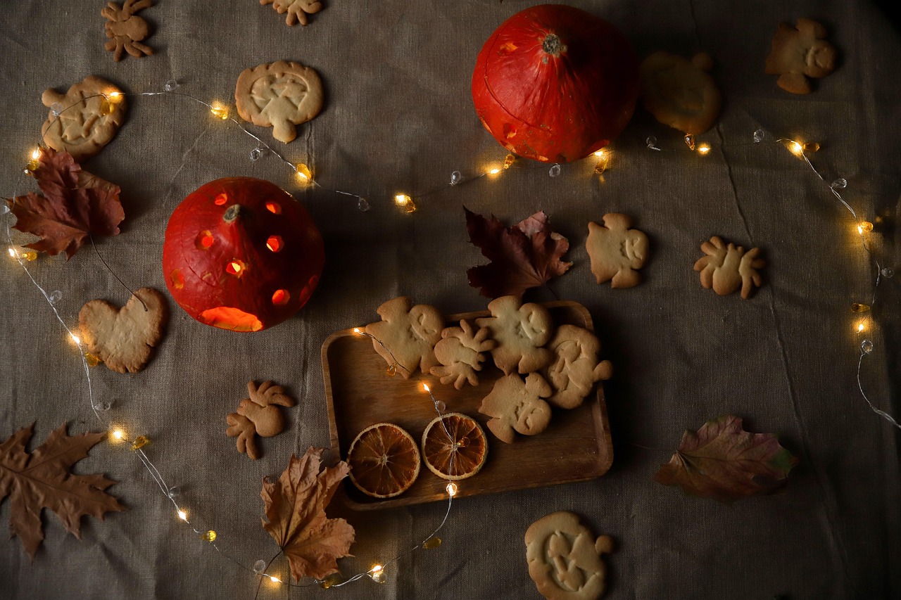 A variety of ghost and pumpkin shaped cookies arranged on a table with autumn leaves and fairy lights.
