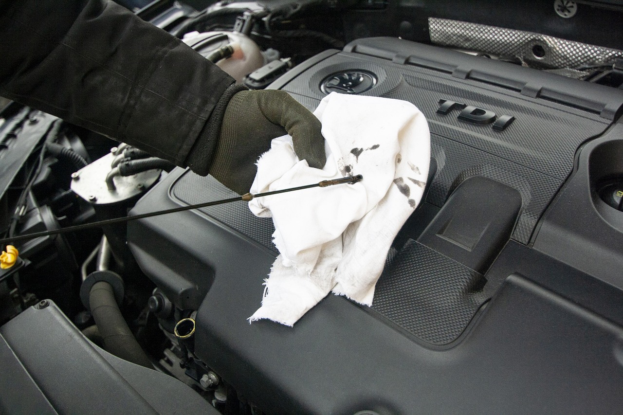 A mechanic's gloved hand checking the oil level of a car engine using a dipstick and a white cloth.