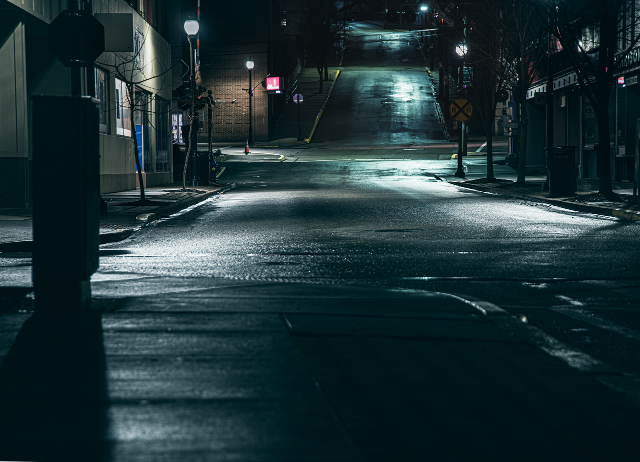 A quiet, dark empty city street at night with wet pavement reflecting streetlights.